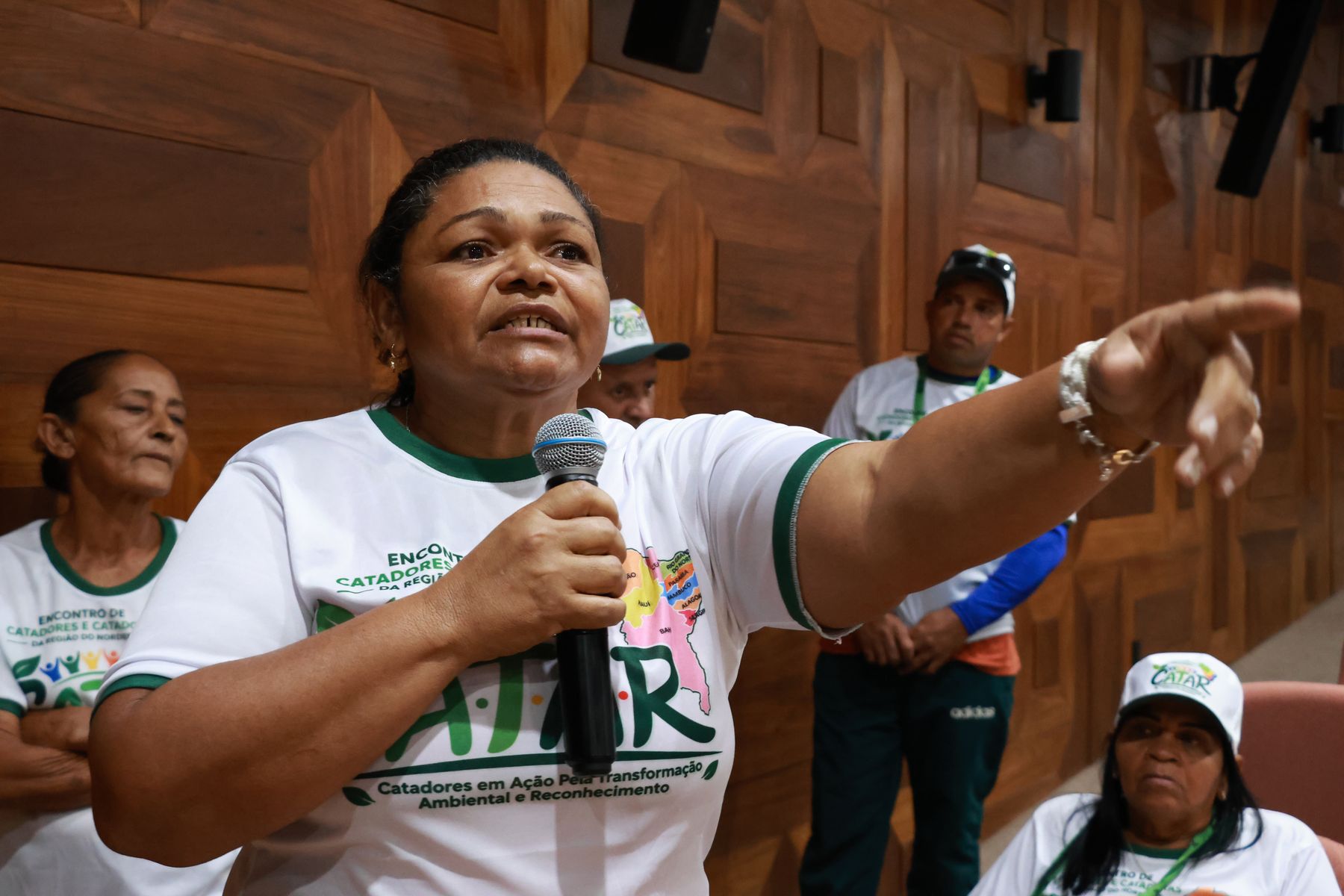 Catadora fala ao microfone e aponta para a plateia