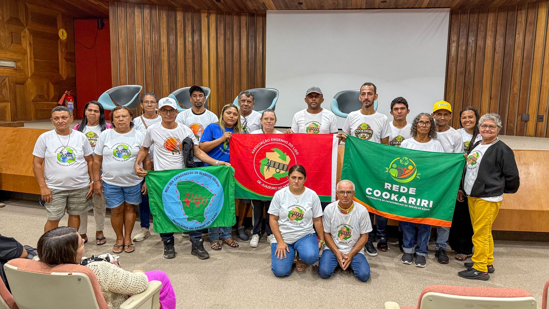 Grupo de catadoras e catadores com as bandeiras das suas organizações no auditório