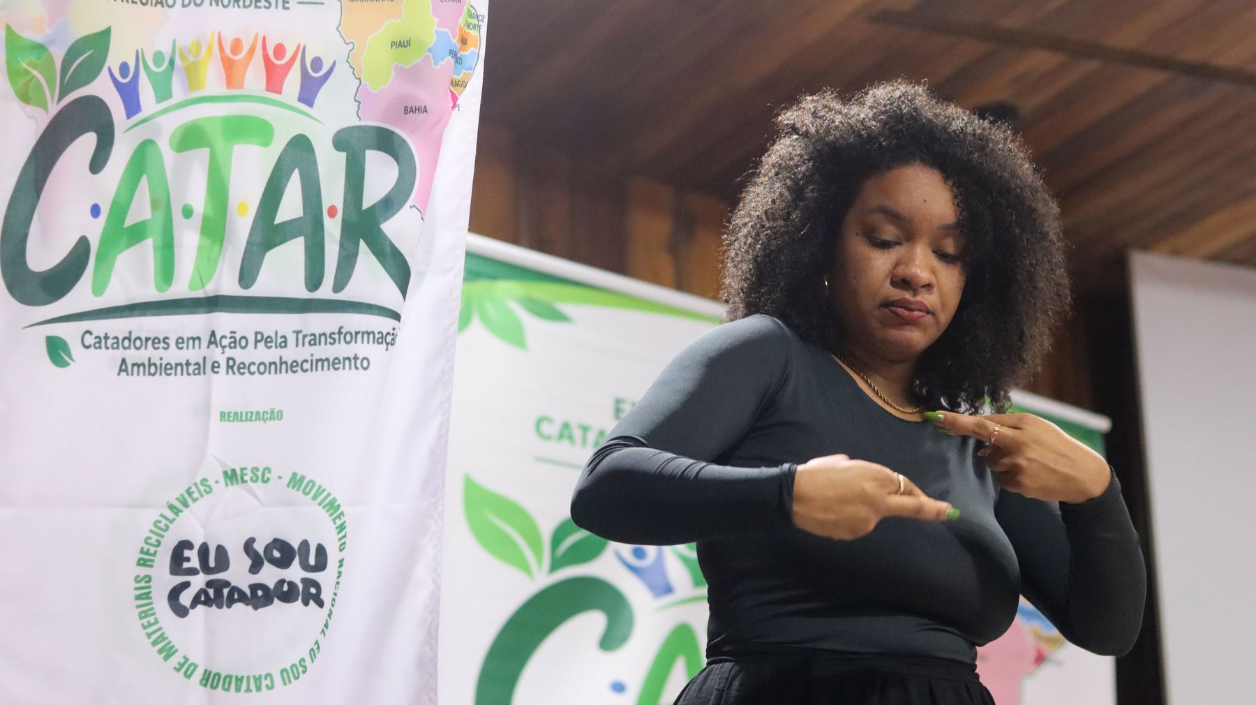 Intérprete de Libras ao lado do banner do CATAR Nordeste