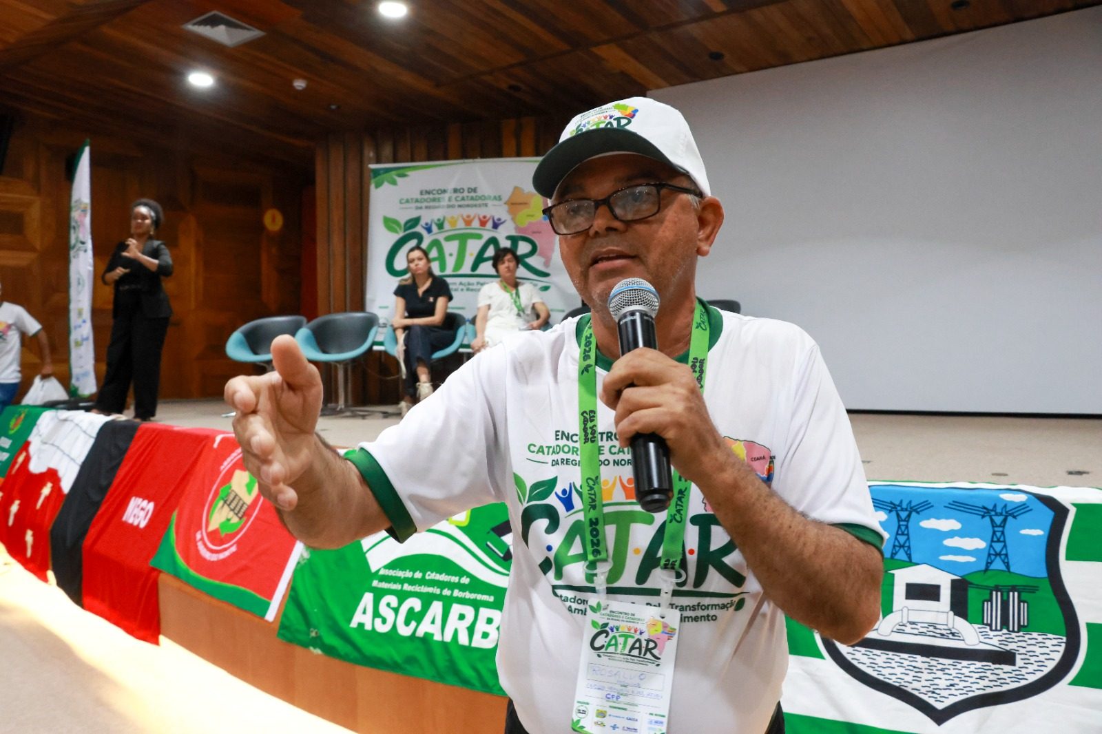 Catador de boné do CATAR fala ao microfone diante das bandeiras das organizações do Nordeste