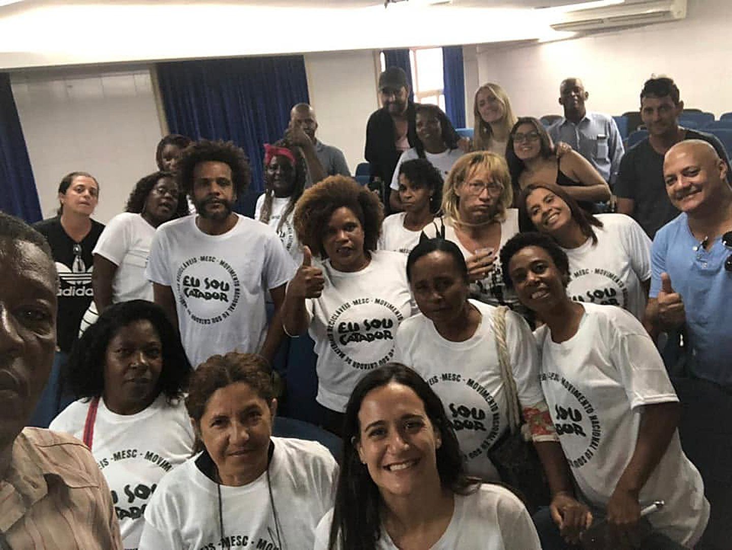 Catadoras e catadores com camisetas Eu Sou Catador reunidos em auditório