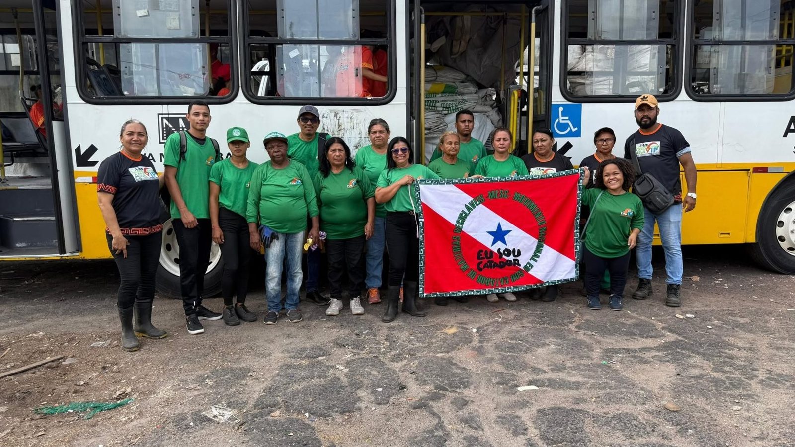 Catadoras de verde com a bandeira do MESC em frente a um ônibus